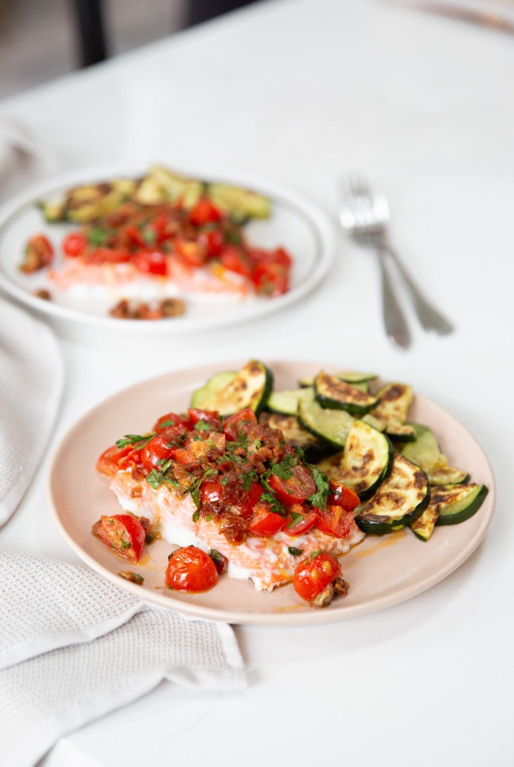 two servings of baked salmon with sun-dried tomato aioli and zucchini on pink and white plates.