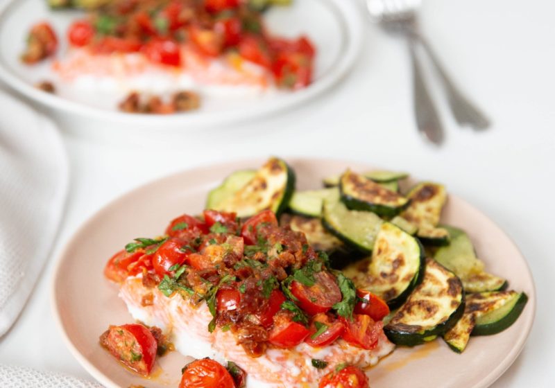 two servings of baked salmon with sun-dried tomato aioli and zucchini on pink and white plates.