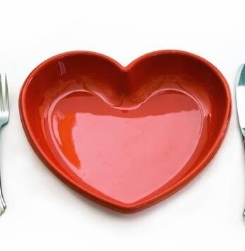 A heart shaped dish between a fork and a knife.
