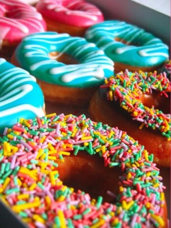 An assortment of donuts. Pink, blue, and rainbow donuts.