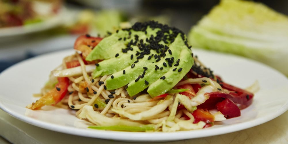 Chilled Noodle Salad with Ginger Wasabi Dressing. Ingredients include ancient grains spaghetti, snow peas, edamame, cucumber, cabbage, pepper, avocado, cilantro, sesame seeds.