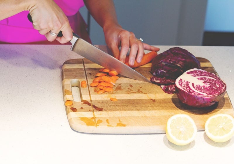 A photo of Registered Dietitian Lindsay Pleskot cutting carrots in the kitchen on a wooden cutting board.