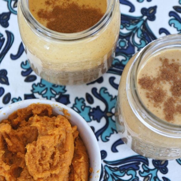 Two Creamy Pumpkin Spice smoothie in mason jars with a bowl of pumpkin puree placed beside them. Ingredients include Greek yogurt, almond milk, almond milk, banana, pumpkin puree, cinnamon, vanilla.