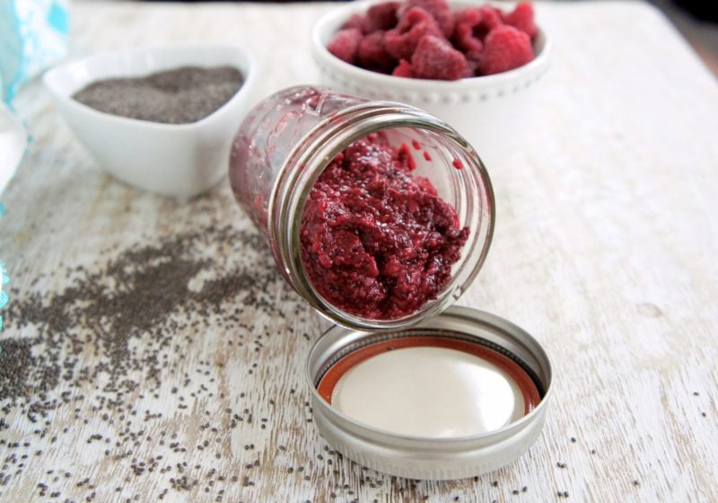 Raspberry chia jam tipped over in a mason jar. Ingredients include chia seeds and raspberries.