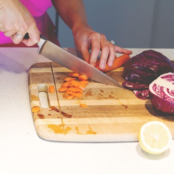 Registered Dietitian Lindsay Pleskot cutting carrots in the kitchen on a wooden cutting board.