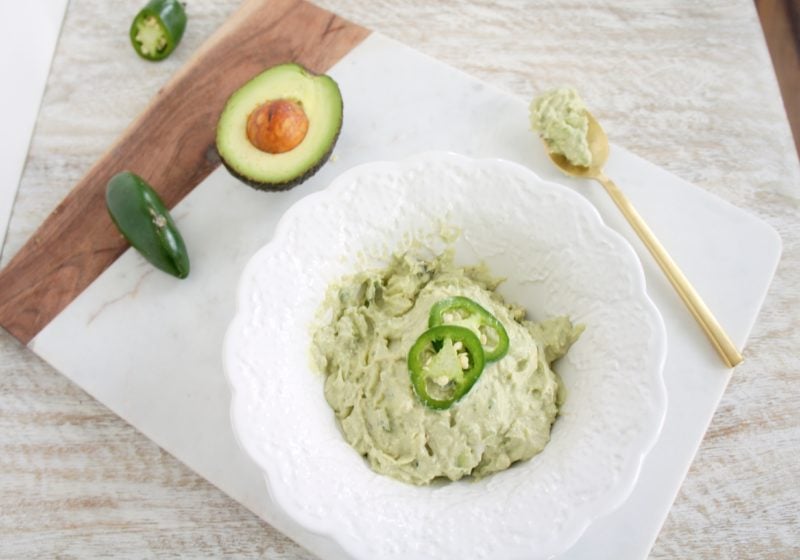 Fresh and Spicy Avopeno Dip in a white serving dish placed on a cutting board. Ingredients include Avocado, Greek yogurt, jalapeno, salt.