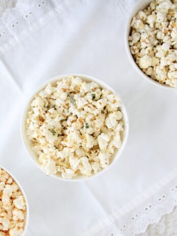 Popcorn three different ways served in white round bowls placed on a white table cloth.