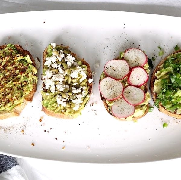 Four versions of avocado toast placed on a white serving plate. Ingredients include sprouted grain bread and avocado.
