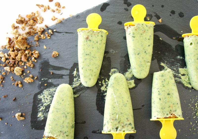 Lime Smoothie Pops placed on a black food photography board. Ingredients include Greek yogurt, kefir, limes, avocado, banana, spinach, granola.