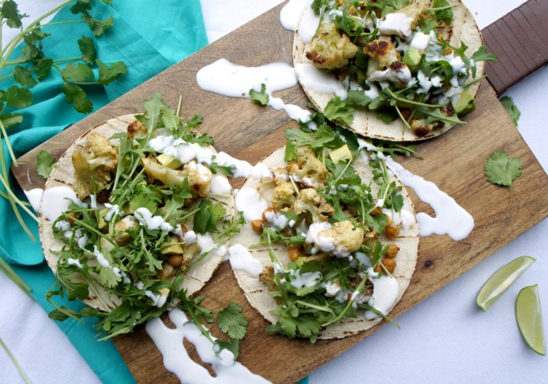 Three Crunchy Roasted Cauliflower Chickpea Tacos placed on a wooden cutting board on top of a blue kitchen towel.