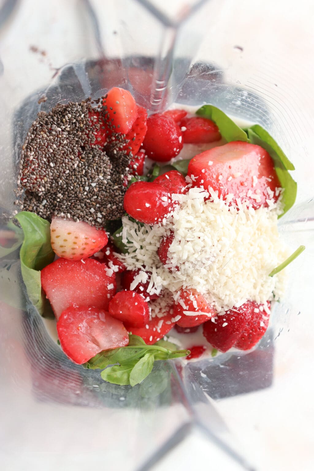 Ingredients for 5 Minute Frozen Strawberry & Basil Smoothie in a blender, including milk, Greek Yogurt, chia seeds, coconut flakes, strawberries, basil, and spinach