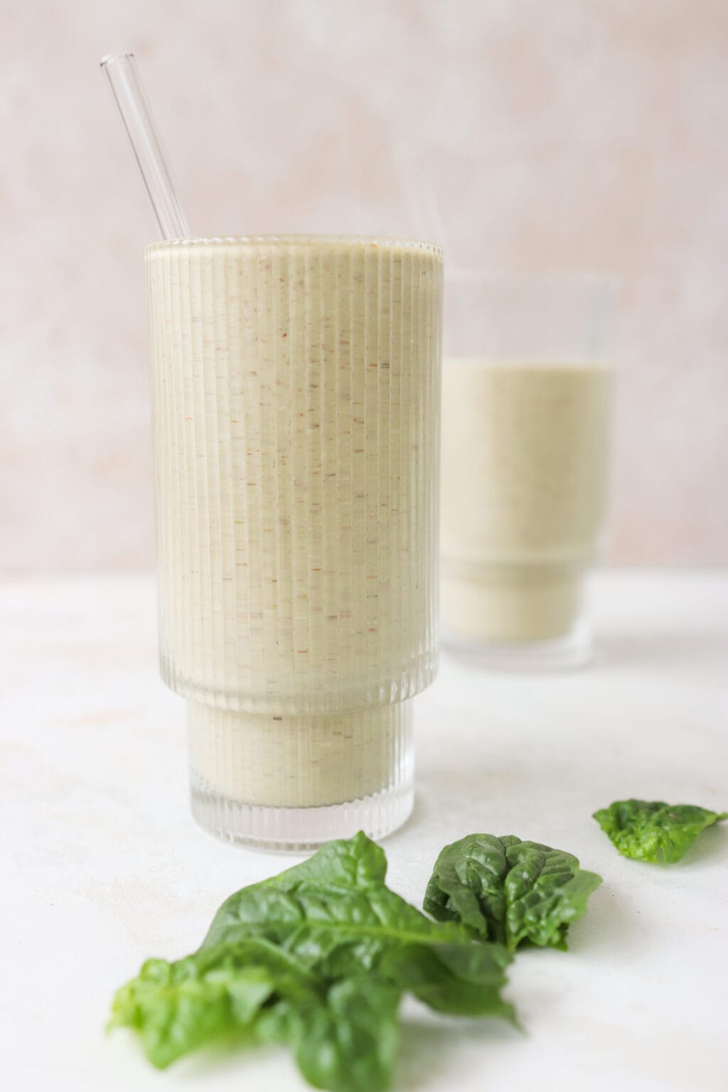 5 Minute Frozen Strawberry & Basil Smoothie in two glass cups on a marble counter with basil leaves lying beside them