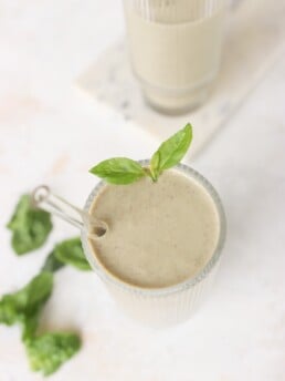 5 Minute Frozen Strawberry & Basil Smoothie in two glass cups on a marble counter with basil leaves lying beside them