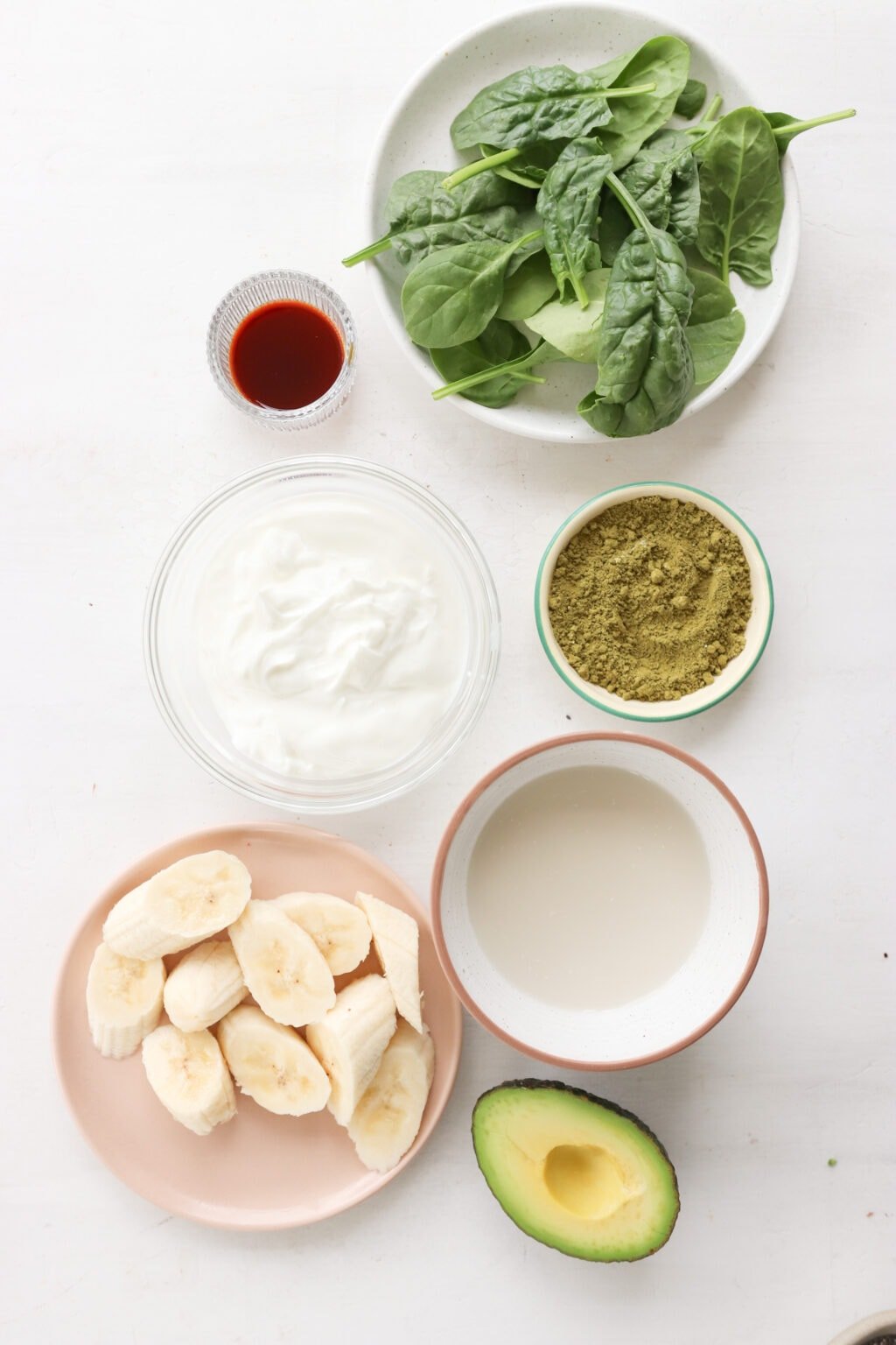 Ingredients for 5-Minute Matcha Smoothie with Banana & Avocado in glass bowls, including milk, matcha powder, avocado, banana, Greek yogurt, greens, vanilla extract