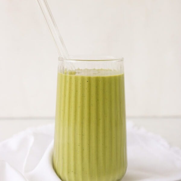 5-Minute Matcha Smoothie with Banana & Avocado in a glass cup with a glass straw and white cloth