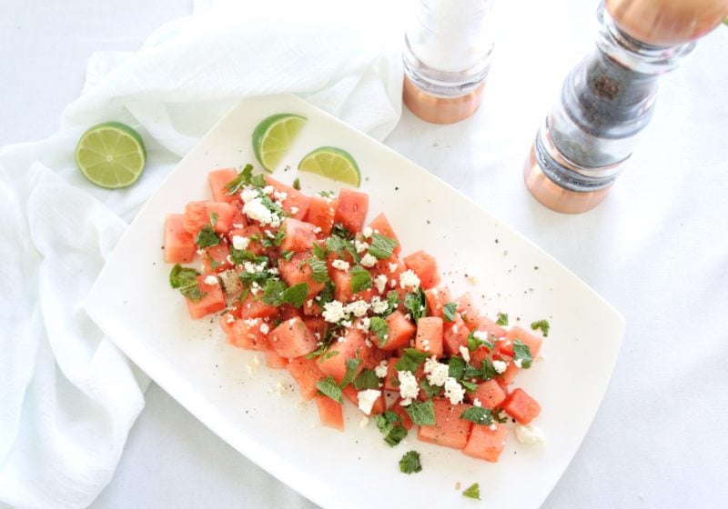Fresh Watermelon, Mint, and Feta Salad placed on a white serving dish with lime wedges and a salt and pepper shaker placed beside it.