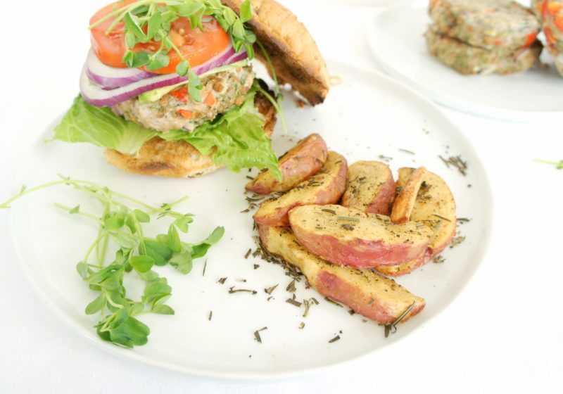 Juicy Greek Turkey Burger placed on a white round plate with a side of potato wedges. Ingredients include ground turkey, garlic, dill, pepper, onion, feta, oregano, whole grain hamburger buns.