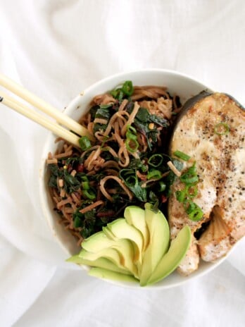 A noodle bowl with chopsticks on a white sheet. Ingredients include noodles, avocado.