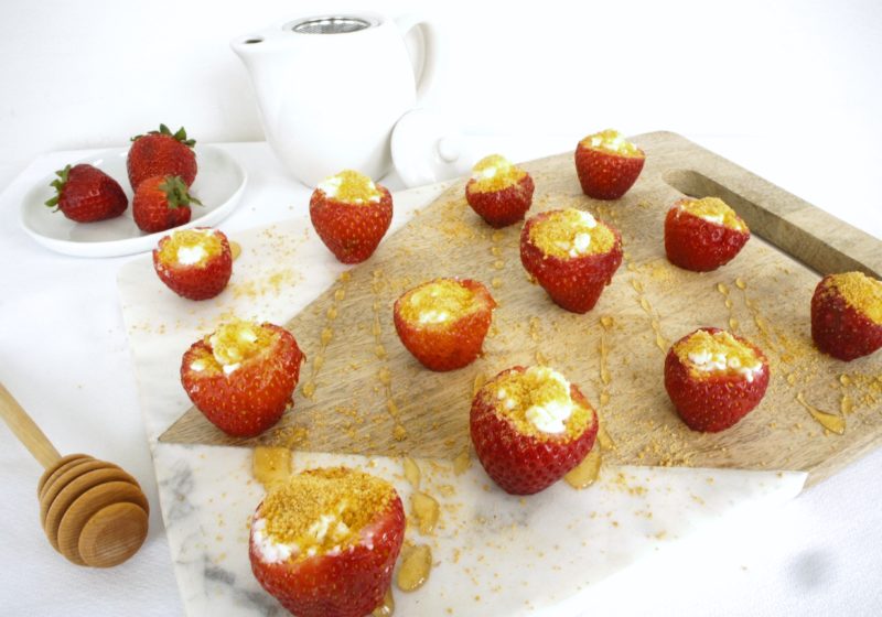 Strawberry Cheesecake Bites placed on a food photography board. Ingredients include strawberries, goat cheese, graham cracker crumbs.