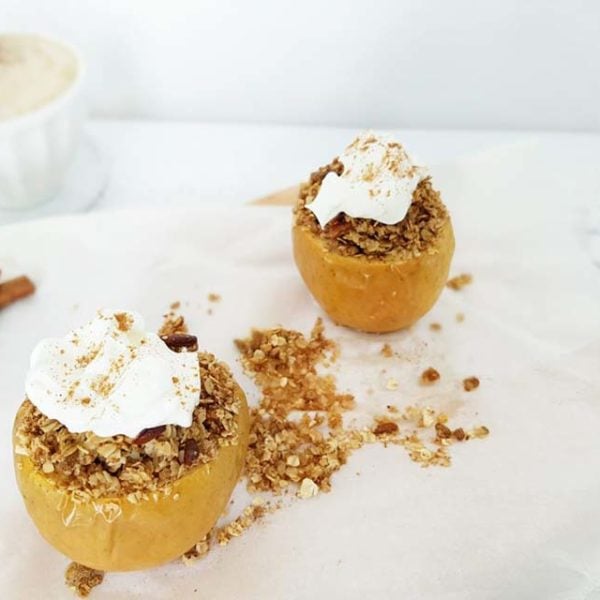 Two Breakfast Apple Crumbles placed on white parchment paper on a white surface. Ingredients include apples, lemon, rolled oats, pecans, cinnamon, Greek yogurt.