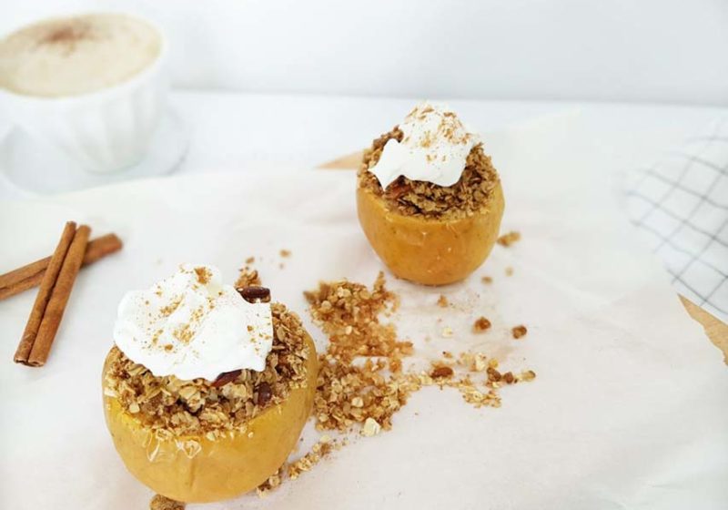 Two Breakfast Apple Crumbles placed on white parchment paper on a white surface. Ingredients include apples, lemon, rolled oats, pecans, cinnamon, Greek yogurt.
