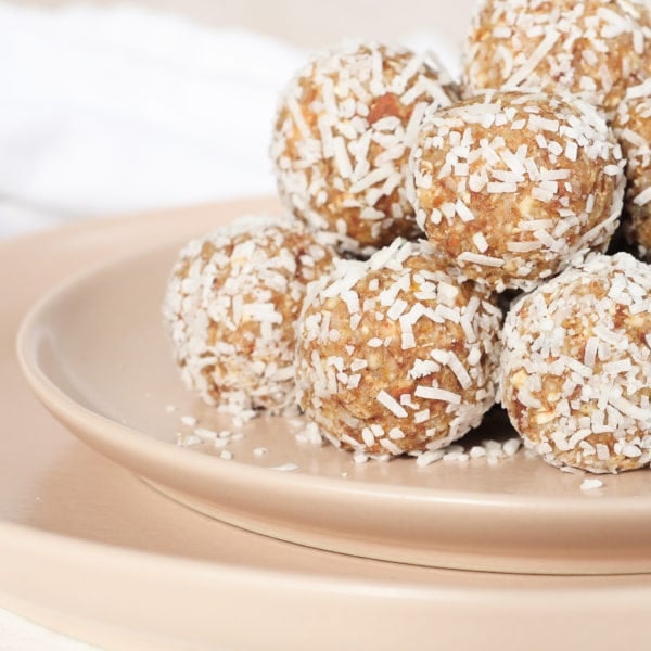 A pyramid of coconut lemon energy balls sit on a pink plate. The image is zoomed in so you only see half of the pyramid. The balls are covered in shredded coconut