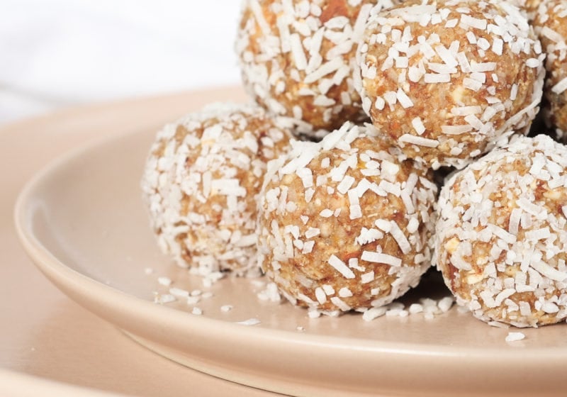 A pyramid of coconut lemon energy balls sit on a pink plate. The image is zoomed in so you only see half of the pyramid. The balls are covered in shredded coconut