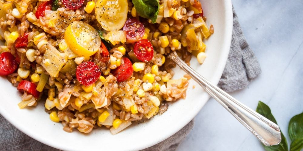 One Pan Faro with Tomatoes, Leeks, and Corn in a white round bowl. Ingredients include water, farro, corn, leeks, garlic, cherry tomatoes, basil, parmesan.