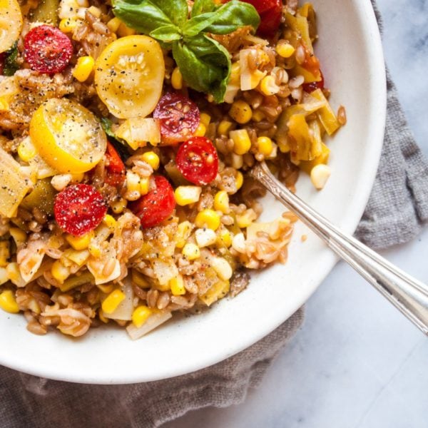 One Pan Faro with Tomatoes, Leeks, and Corn in a white round bowl. Ingredients include water, farro, corn, leeks, garlic, cherry tomatoes, basil, parmesan.