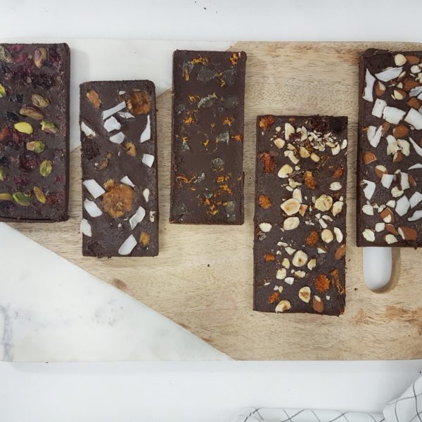 DIY Fruit, Nut and Flower Laced Chocolate Bars placed on a cutting board. Ingredients include chocolate, coconut oil, fruit, flowers.