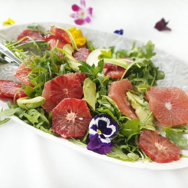 Refreshing Citrus Salad with Blood Orange and Mint placed on a white serving plate. Ingredients include mixed greens, fresh mint, oranges, grapefruit, avocado.