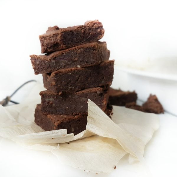 Genuine(ly) Health(ly) Sweet Potato Protein Brownies placed on a white counter on top of parchment paper. Ingredients include yam, almond meal, cacao, oat flour, vegan fermented protein, dates.