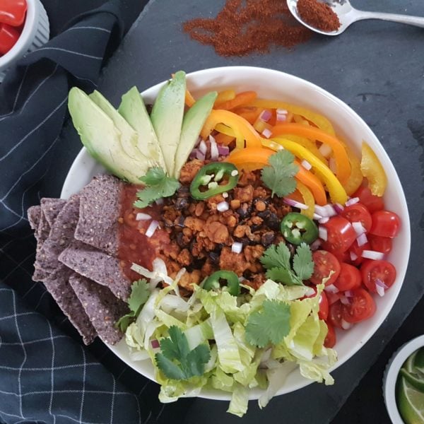 Fiesta Tempeh Taco Bowls placed in a white round bowl. Ingredients include rice, garlic, black beans, chili, paprika, cumin, bell pepper, onion, lettuce.