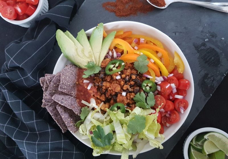 Fiesta Tempeh Taco Bowls placed in a white round bowl. Ingredients include rice, garlic, black beans, chili, paprika, cumin, bell pepper, onion, lettuce.