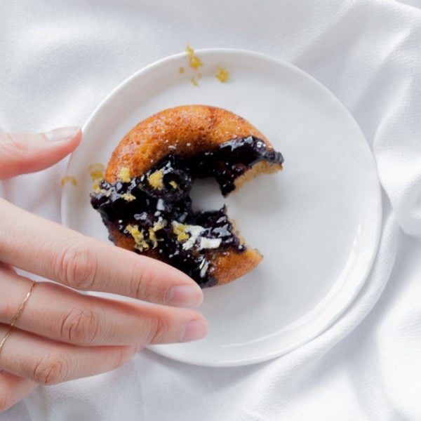 Registered Dietitian Lindsay Pleskot reaching for a donut placed on a white round plate over a white surface.