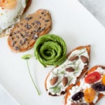 4 baked sweet potato toasts placed on a white serving plate with avocado art in the middle. Ingredients include sweet potato, peanut butter, avocado, fried egg, cottage cheese.