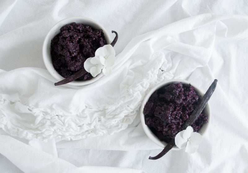 Two white bowls filled with Violet Rice Pudding on a white surface with white kitchen towels. Ingredients include violet rice, almond milk, vanilla beans.