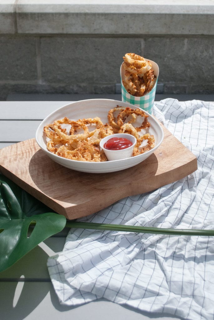 A bowl of oven-baked, Panko crusted onion rings on a patio table in the sun.