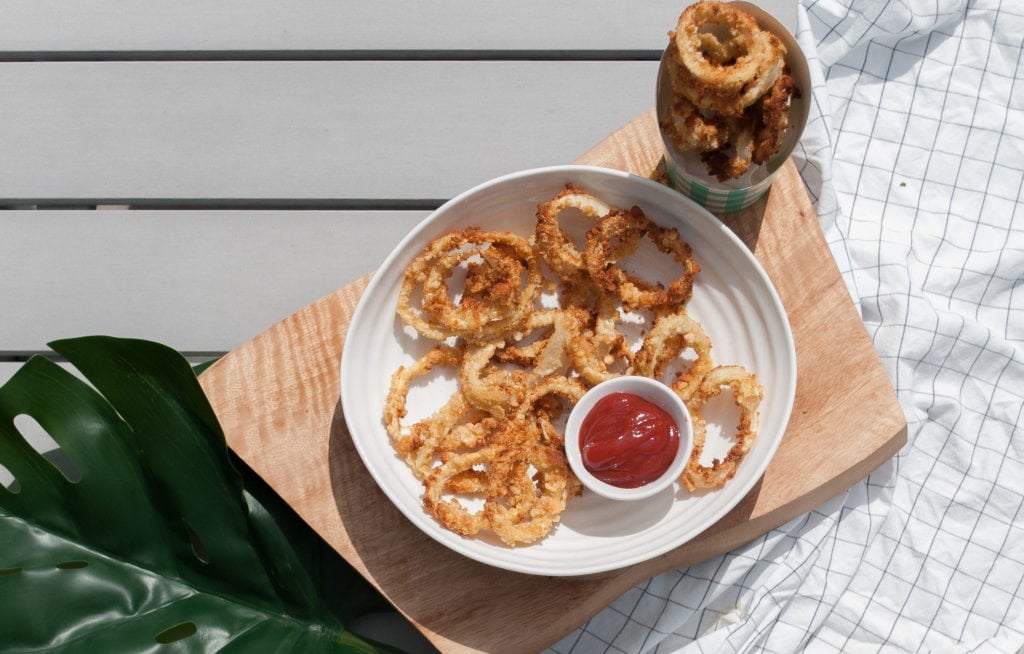 Homemade onion rings and dipping sauce in a white bowl on a patio table in the sun