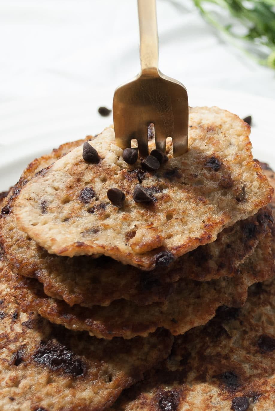 A gold form is stabbing through a stack of 5 banana pancakes. The pancakes have chocolate chips in the and are browned perfectly.