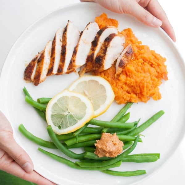Registered Dietitian Lindsay Pleskot holding a white round plate with chicken, mashed yam, lemon slices, and green beans.