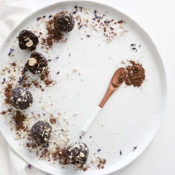 A round white plate topped with Healthy Ferrero Rocher Energy Bites on a white surface with a white kitchen towel. Ingredients include dates, hazelnuts, cacao, sea salt.
