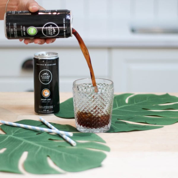 A can of coffee being poured into a drinking glass with two large leaves placed around it.