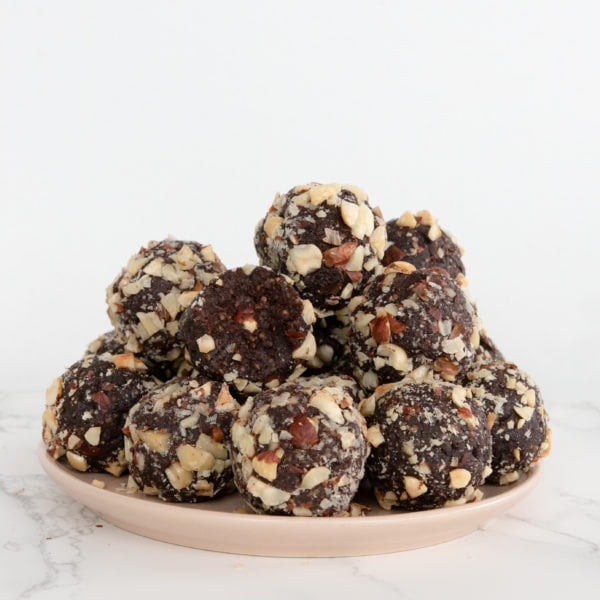 A pile of hazelnut, chocolate energy balls sits on a pink plate on a marble counter top.