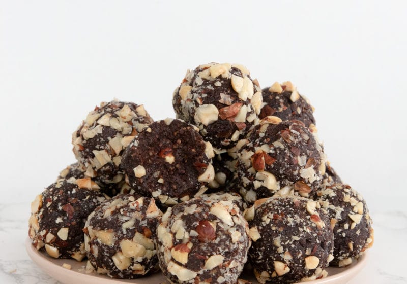 A pile of hazelnut, chocolate energy balls sits on a pink plate on a marble counter top.