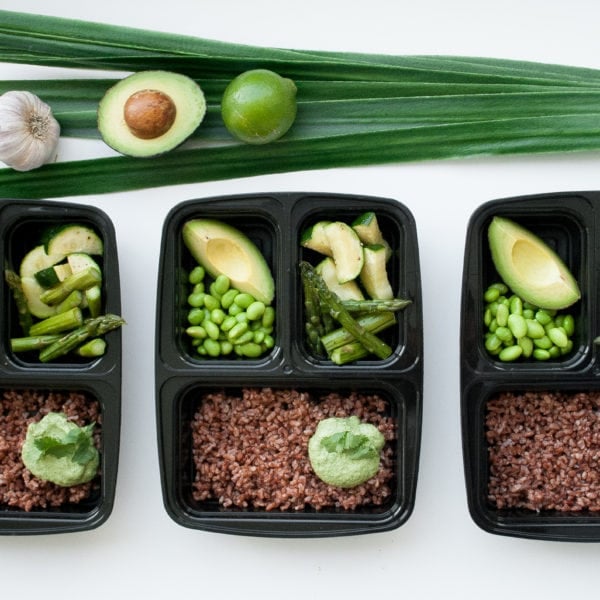 Three meal prep containers fillled with rice, avocado, edamame, asparagus, garlic, lime, leek.