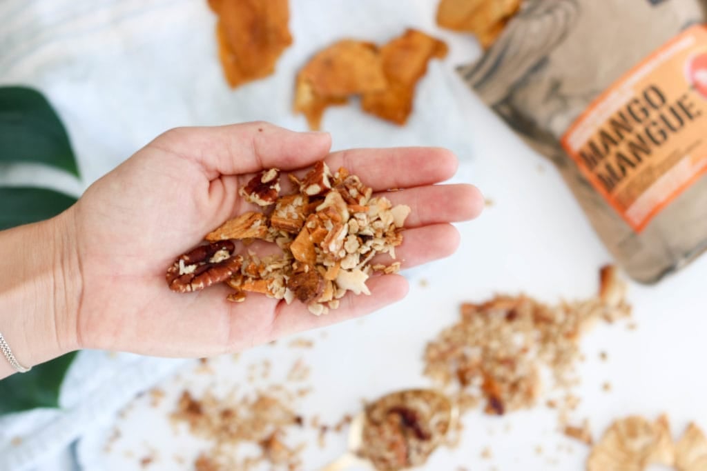 Lindsay Pleskot's holding a handful of Crunchy & Nutritious Coconut Granola. Ingredients include: coconut oil, honey, rolled oats, chia seeds, pecans, walnuts, coconut pieces, dried mango and pineapple. 