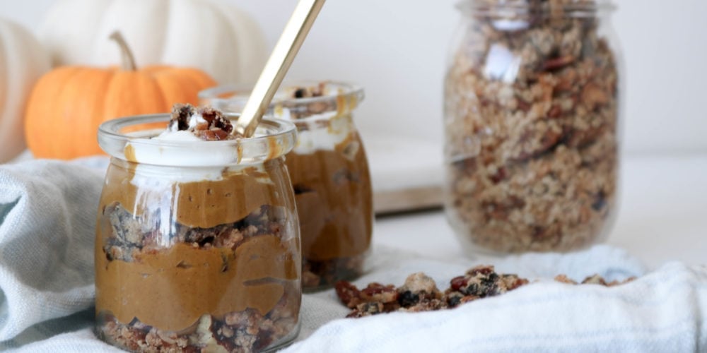 Two jars filled with Deconstructed Pumpkin Pie on a counter with a white kitchen towel and a jar of granola and pumpkins in the background. Ingredients include pumpkin, nut milk, prunes, maple syrup, vanilla.