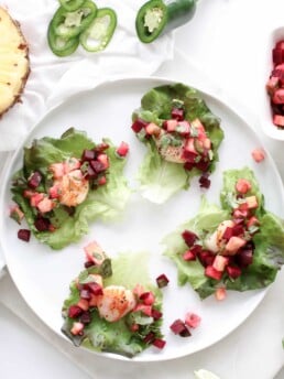 A white round place on a white surface topped with three lettuce leafs topped with scallops.