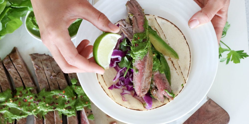Registered Dietitian Lindsay Pleskot holding a lime wedge over a round white plate topped with grilled steak chimichurri.